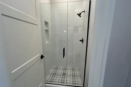 Installer aligning frameless shower glass panel in modern tiled bathroom