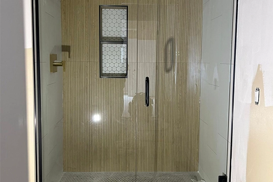 Glass shower enclosure with wooden textured wall and hexagonal window.